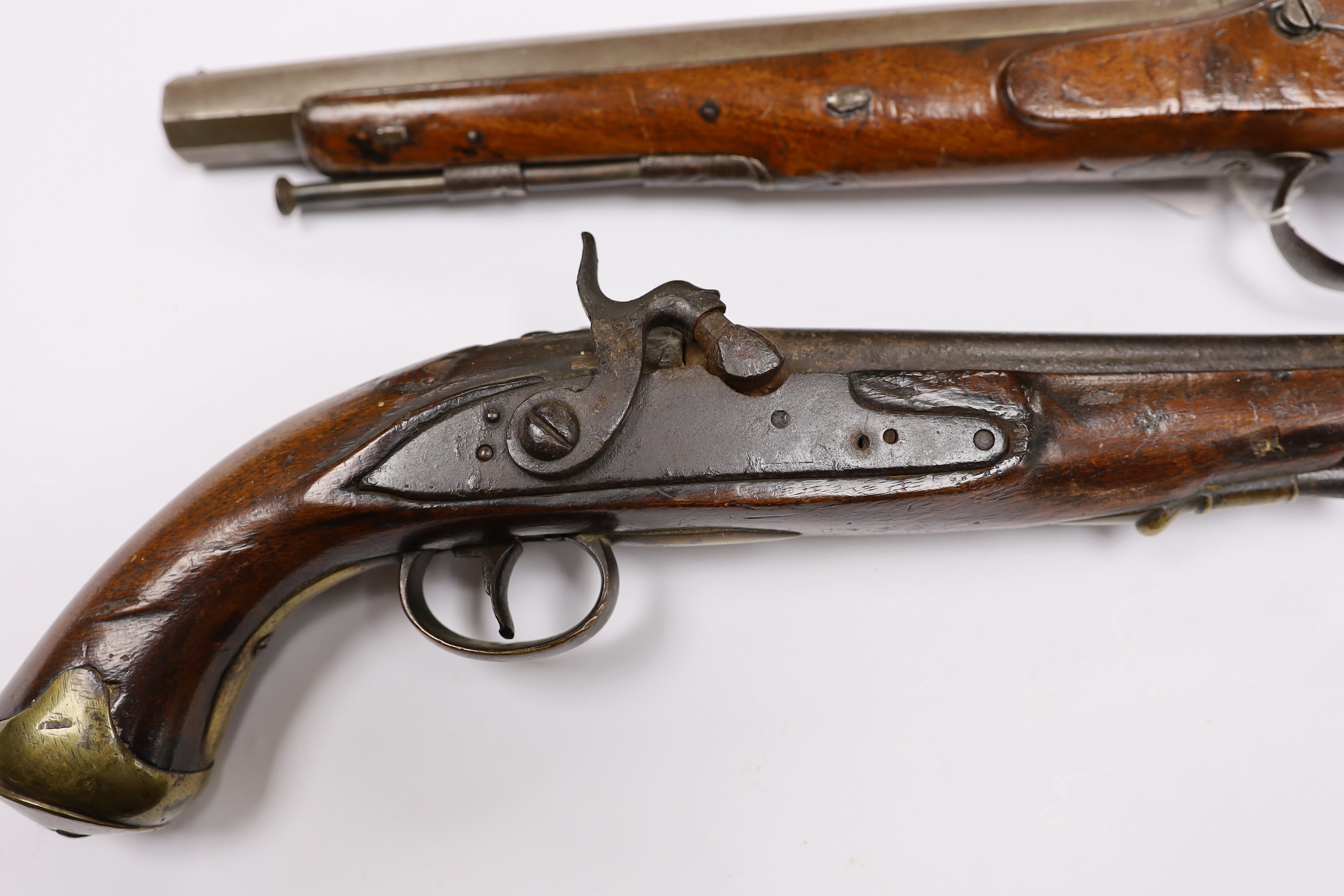 Two percussion 19th century pistols, both converted from flintlock, the larger example with engraved lock and hammer, octagonal barrel and chequered grip, together with a smaller overcoat pistol, fully stocked with brass